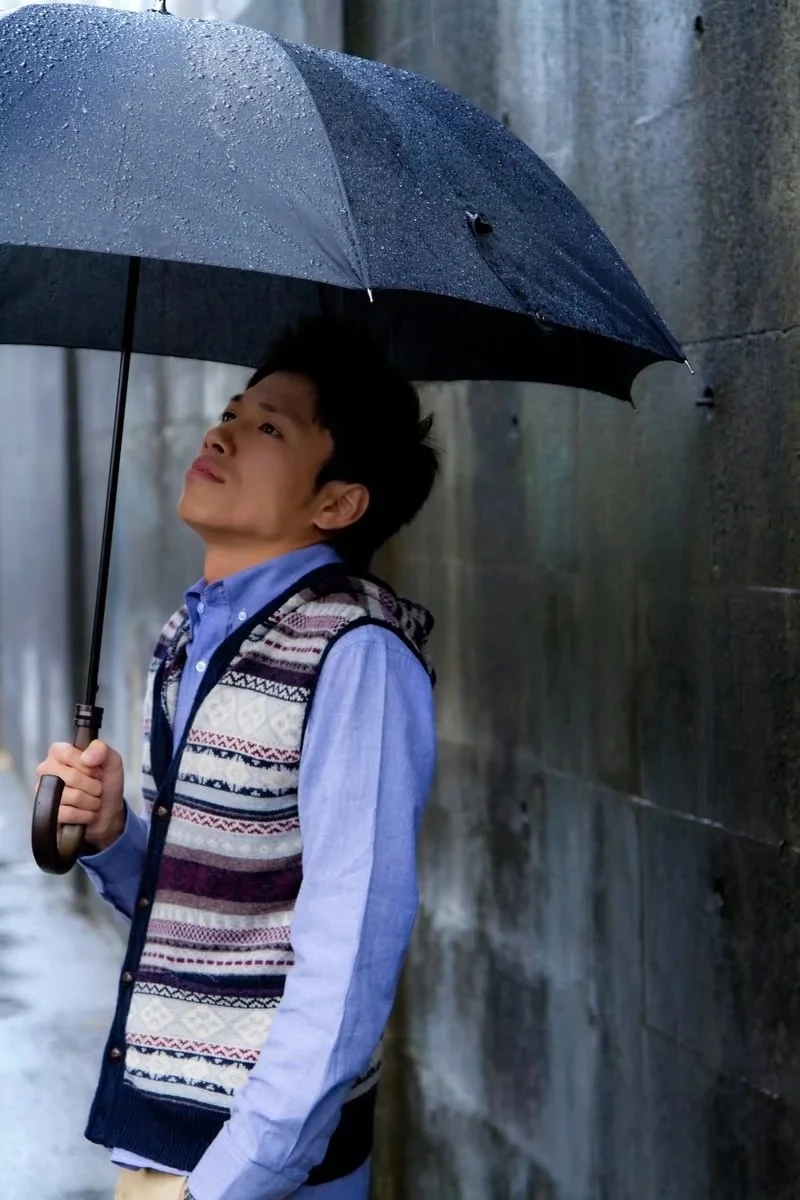 雨の中で傘を差し空を見上げる男性