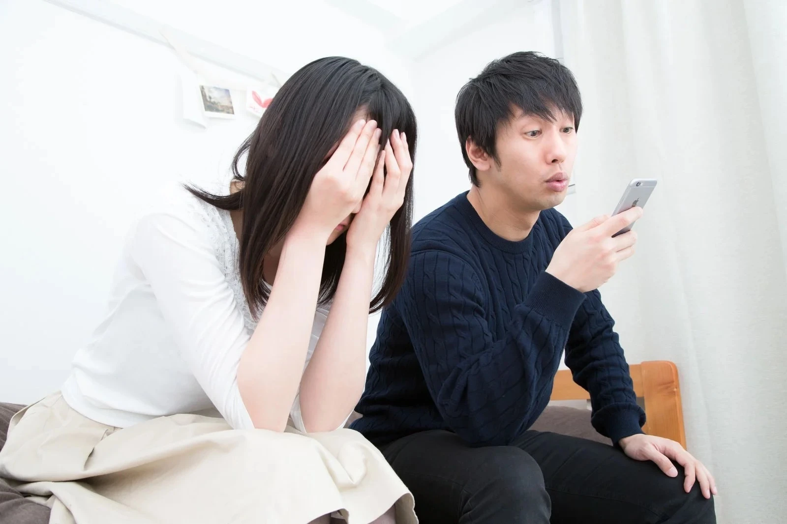 顔を掌で覆う女性と隣りでスマホを見る男性