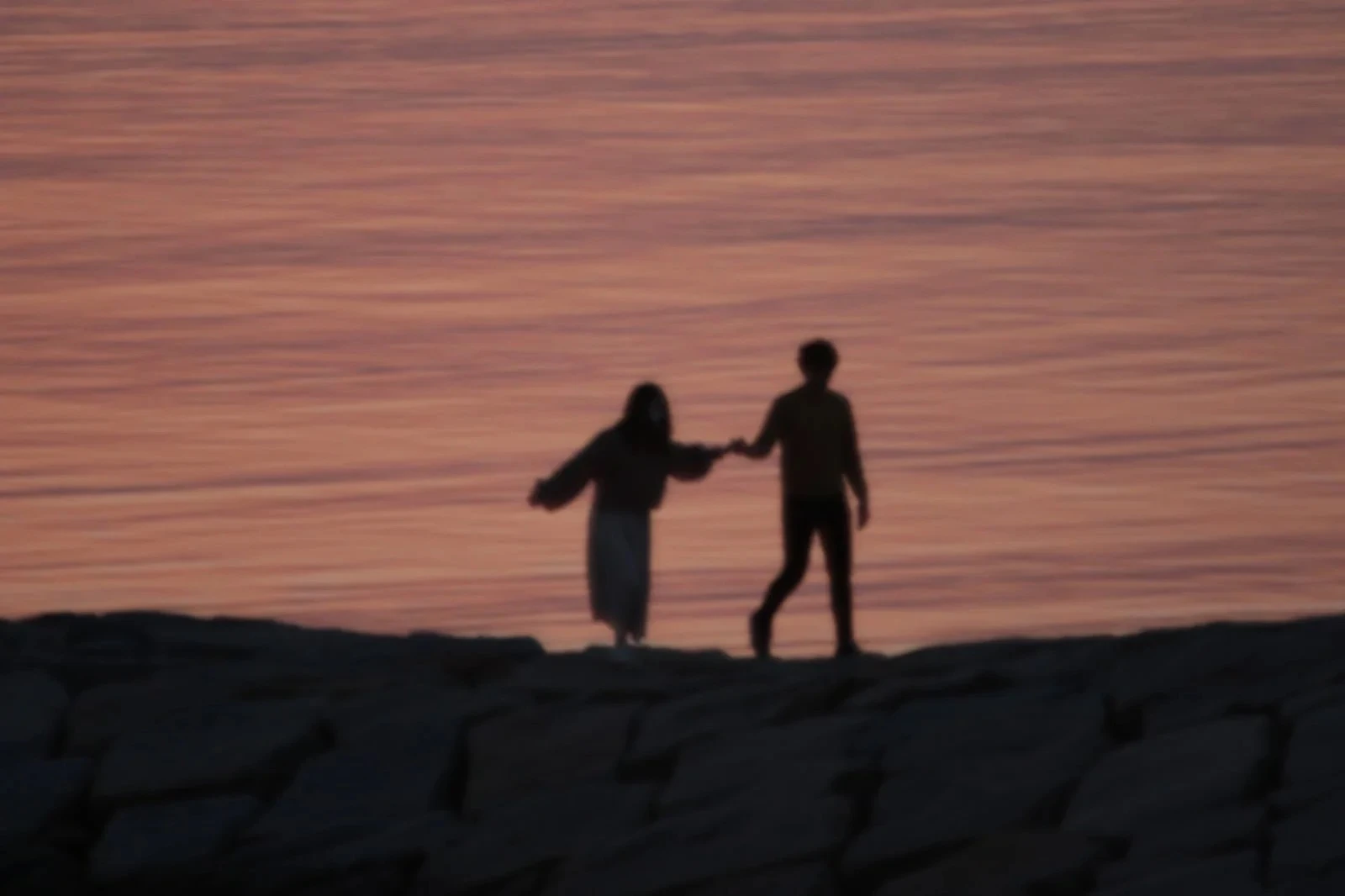 夕日を浴び渚を歩く男女のシルエット