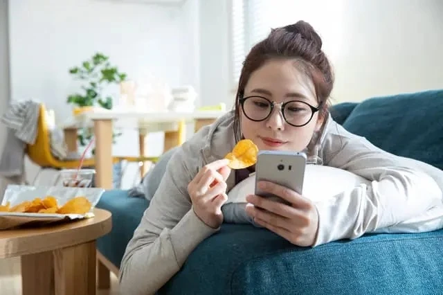 寝そべりお菓子を片手にスマホに夢中の若い女性