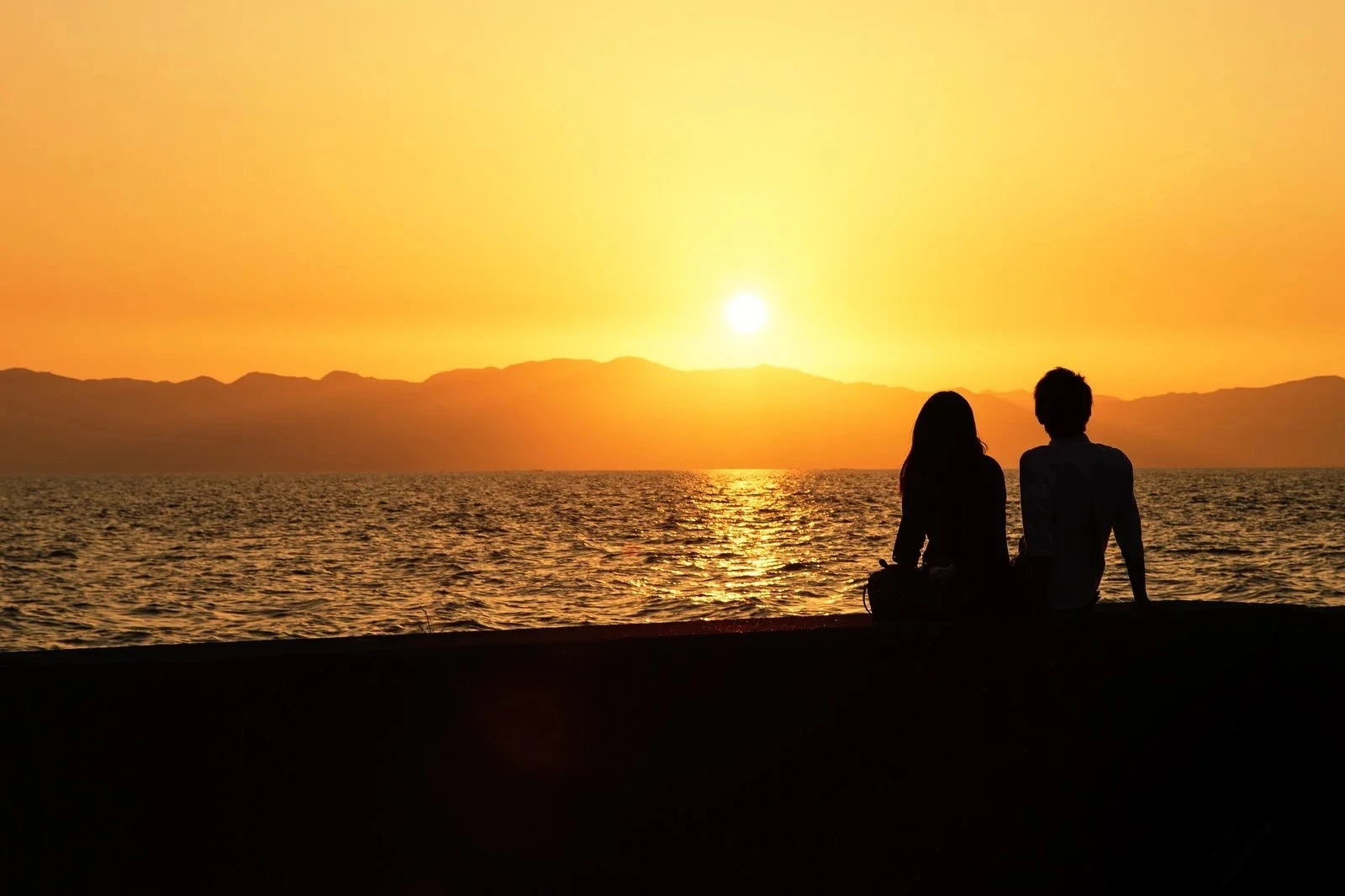 海辺で夕陽を見ながら語り合う男女のシルエット