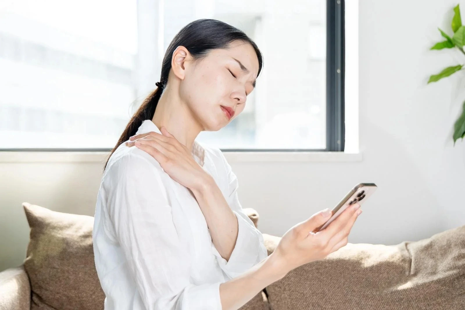 肩をさすりながらスマホを眺める女性