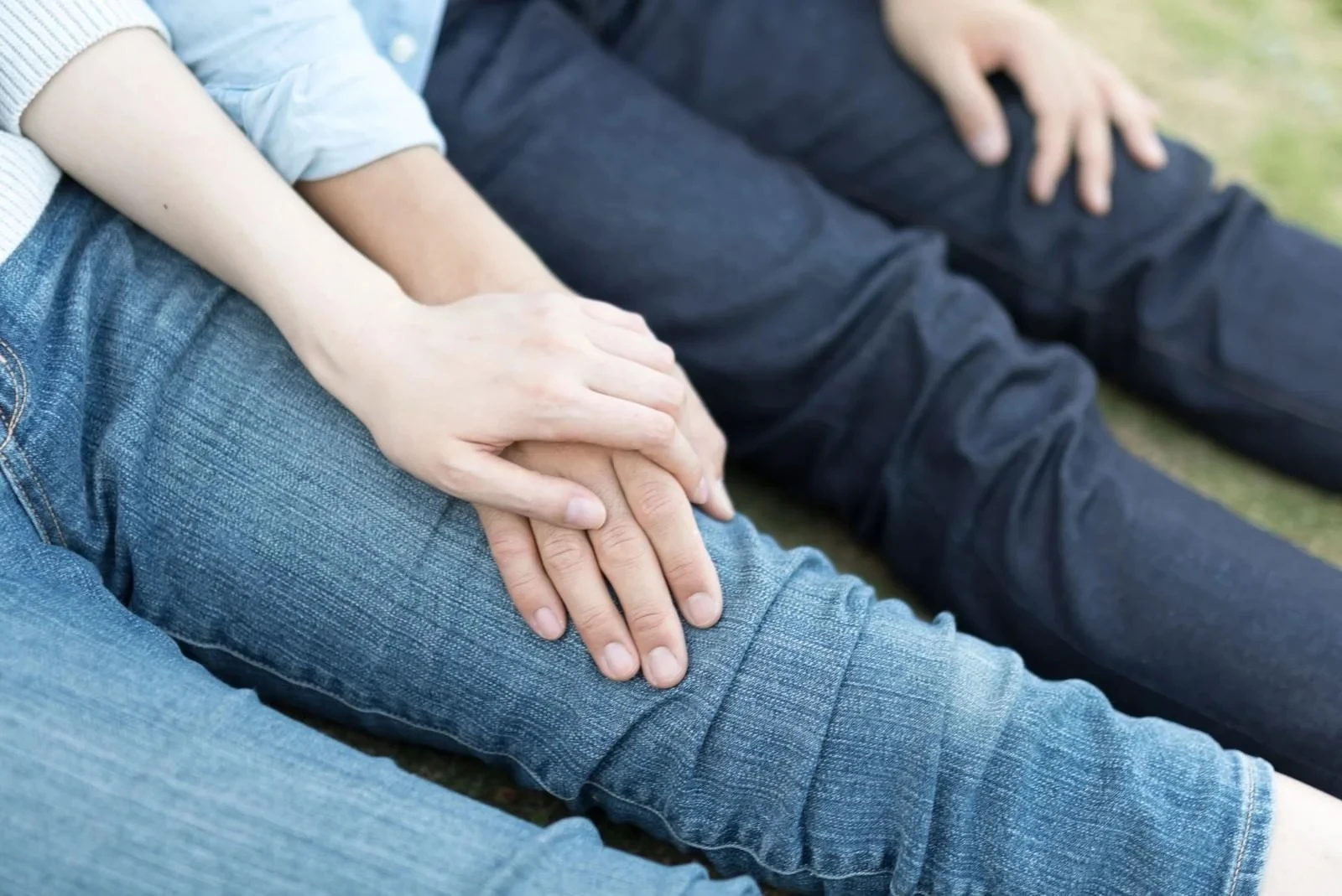 一緒に芝生に座って掌と掌を重ねあうカップル