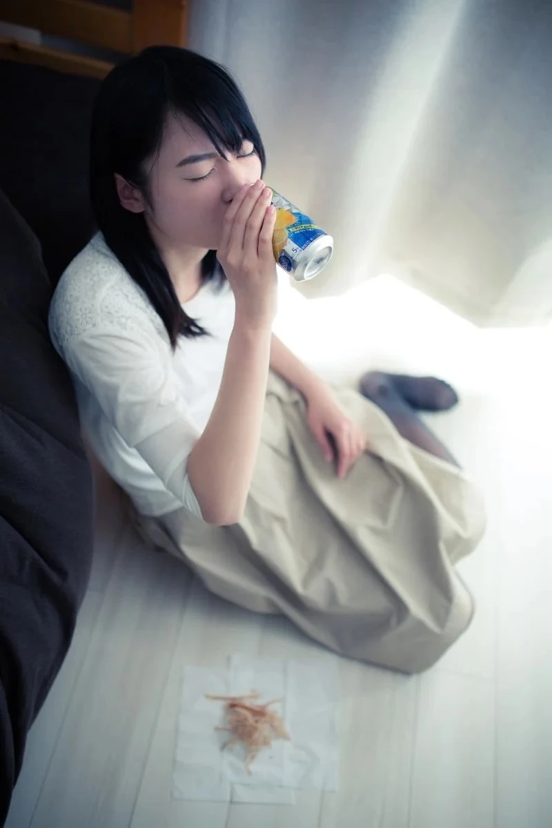 床に座ってヤケ酒を飲む若い女性